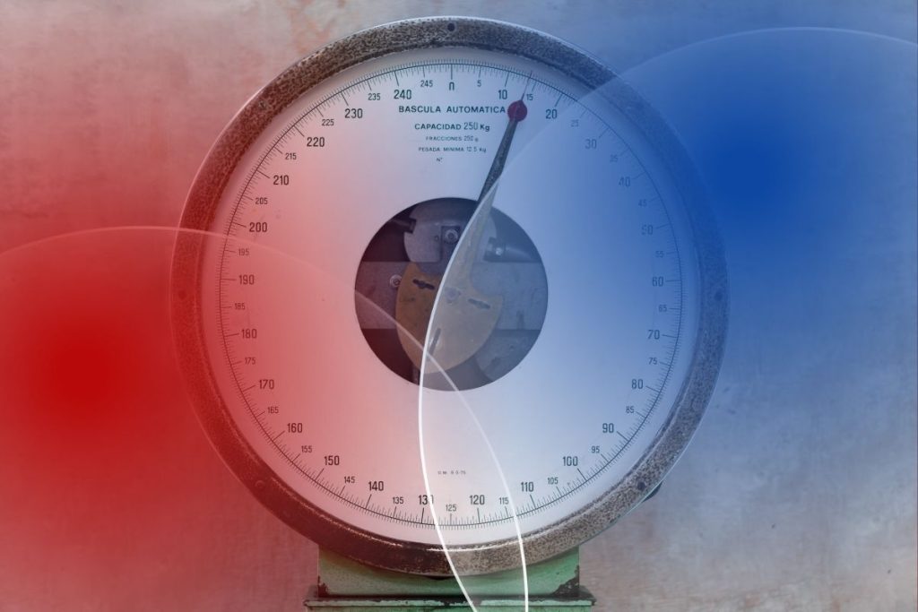 Zbliżenie na tarczę starej wagi przemysłowej. Czerwone i niebieskie nakładki symbolizują czynniki zakłócające, które są najczęstszą przyczyną błędnych pomiarów wag.